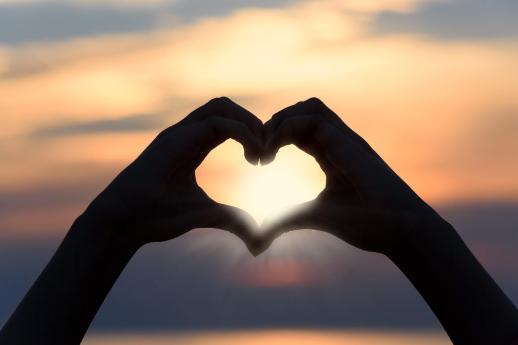 two hands in the shape of a heart with a sunset