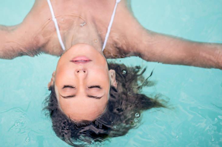 Woman wearing white swimsuit floating on her back in a turquoise swimming pool